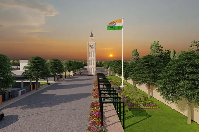 Scenic view of Mansha Heritage project's central boulevard featuring a prominent clock tower, Indian flag, landscaped flower beds, and lush greenery at sunset